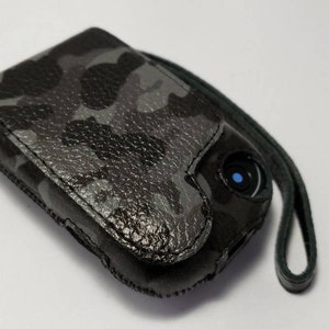 May include: A black and gray camouflage leather phone case with a black strap.