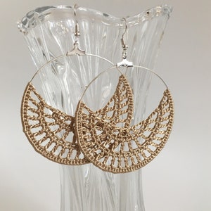 May include: A pair of gold crocheted hoop earrings with silver hooks. The earrings are large and have a delicate, intricate design.