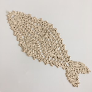 Può includere: Un runner da tavolo in crochet beige a forma di pesce con un delicato motivo a pizzo.
