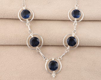 May include: A silver necklace with six dark blue gemstones in circular settings. The necklace has a fine chain and connecting bars. The gemstones are evenly spaced, creating a symmetrical design. The necklace is a piece of jewellery.