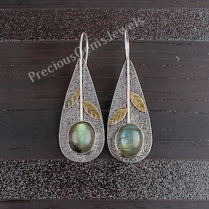 May include: Silver teardrop earrings with a textured finish and a round green gemstone. Each earring features two gold leaf accents.