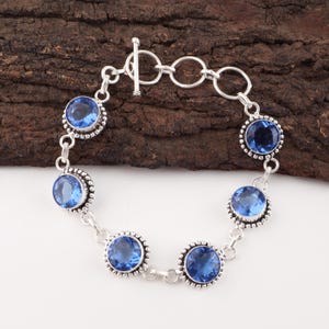 Può includere: Un bracciale in argento con sei pietre preziose blu rotonde e sfaccettate. Ogni gemma è incastonata in una lunetta decorativa con un bordo perlato. Il bracciale ha una chiusura a toggle.