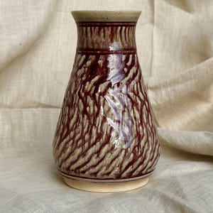 May include: A handmade ceramic vase with a textured, reddish-brown and beige design. The vase has a wide base, a slightly flared body, and a narrow neck. The rim and base are a lighter beige color.
