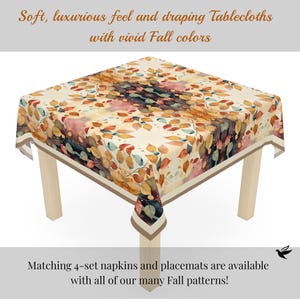 May include: A square tablecloth featuring a pattern of autumn leaves in shades of orange, yellow, red, and dark blue on a cream background. The text on the image reads: Soft, luxurious feel and draping Tablecloths with vivid Fall colours.