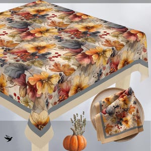 May include: A square tablecloth and a matching folded napkin featuring a botanical print of orange flowers, brown and grey autumn leaves, and small red berries on a cream background, finished with a wide grey and beige border trim.