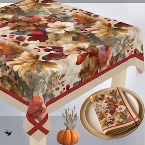 May include: A rectangular tablecloth and a matching folded napkin featuring a pattern of autumn leaves, white flowers, and red berries on a cream background with a solid red border. A small orange pumpkin sits near the table corner.