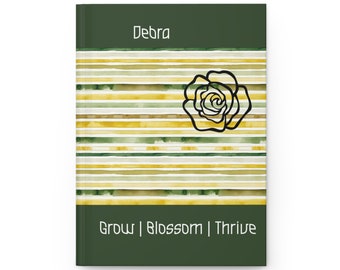 May include: A green journal with a watercolor striped pattern in yellow and green. The journal has a black rose design and the text "Debra Grow | Blossom | Thrive" on the front cover.