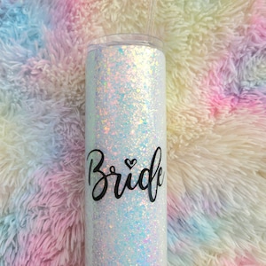May include: A white iridescent glitter tumbler with a black vinyl decal that says "Bride" with a small heart above the "d".