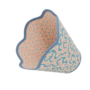 Puede incluir: Un artículo de tela decorativo con borde azul y borde festoneado. El interior presenta un patrón de pequeños puntos rojos y azules sobre un fondo crema. El exterior muestra un diseño de coral azul y rojo.