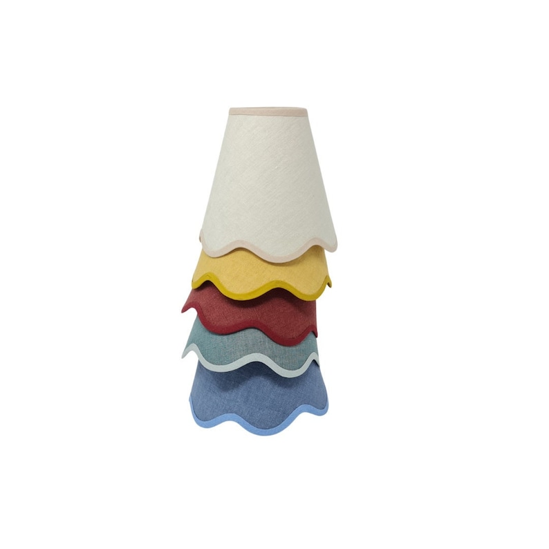 May include: A stack of five lampshades in various colors. The top shade is white, followed by yellow, red, blue, and light blue. All shades have a scalloped edge.