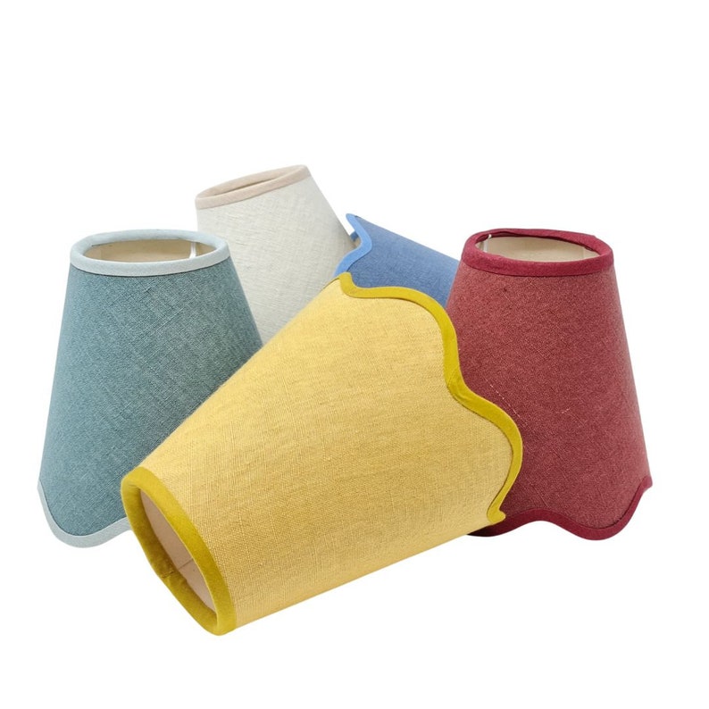 May include: Four lampshades in different colors: light blue, beige, yellow, and red. Each lampshade has a scalloped edge and a contrasting trim.
