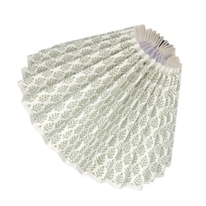 May include: A white fabric lampshade with a green leaf pattern. The lampshade is pleated and has a white trim.