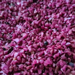 Könnte beinhalten: Nahaufnahme eines Haufens kleiner, unregelmäßig geformter, tiefroter Edelsteine. Die Edelsteine sind über die Oberfläche verstreut und erzeugen eine strukturierte und visuell reiche Darstellung. Die Farbe ist durchgehend, mit Variationen in Licht und Schatten.