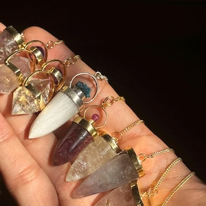 May include: A set of seven crystal point pendulums with gold chains. The pendulums are made of clear quartz, amethyst, rose quartz, smoky quartz, clear quartz with gold flecks, white quartz, and red jasper.