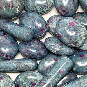 Peut inclure: Un ensemble de pierres précieuses polies de différentes formes, dont des ovales et des cylindres. Les pierres ont une couleur de base bleu-vert avec des inclusions rouge foncé et vertes, créant un effet marbré. L'arrangement est en gros plan, mettant en valeur les motifs naturels.