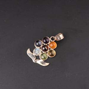 May include: Silver pendant featuring a cluster of seven colorful gemstones. The gemstones are arranged in a grape-like pattern, with a variety of colors including blue, purple, orange, and green. The pendant has a decorative, curved silver design.