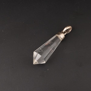 May include: A clear quartz crystal pendant with a silver-coloured bail. The crystal is faceted, with a pointed end and a hexagonal shape. The pendant is displayed against a dark background.