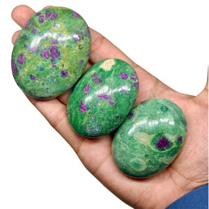 May include: Three polished oval stones featuring a vibrant green base colour with embedded deep magenta and purple crystalline inclusions. The stones have a smooth, glossy surface texture and display natural variations in colour and pattern throughout.