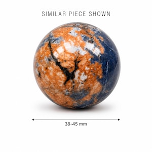 Può includere: Una pietra sferica lucida con un motivo marmorizzato di blu profondo, arancione vivace e venature nere. Il testo SIMILAR PIECE SHOWN appare sopra e una linea di misurazione sottostante indica una dimensione di 38-45 mm.