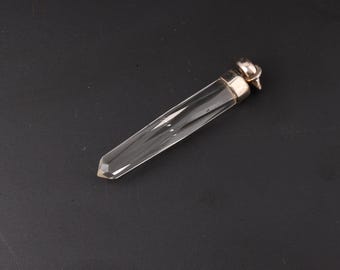 May include: A clear, faceted crystal vial with a silver-colored cap. The vial is elongated and tapers to a point. The cap has a small, decorative element. The vial is set against a dark background.