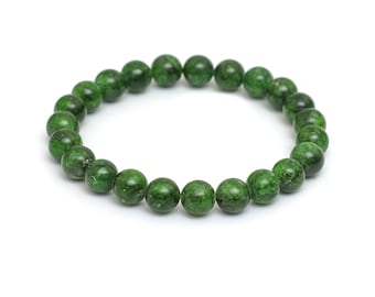 May include: A green beaded bracelet. The bracelet is made of round, polished beads in varying shades of green. The beads are strung together to form a complete circle, resting on a white background.