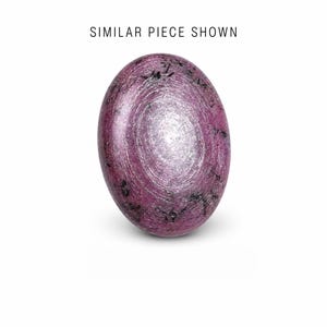 Puede incluir: Una piedra ovalada pulida con un patrón arremolinado en tonos morados y plateados. La piedra tiene motas oscuras y se muestra sobre un fondo blanco. El texto "SIMILAR PIECE SHOWN" es visible en la parte superior.
