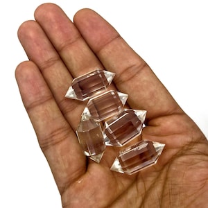 May include: Five clear quartz double terminated points, also known as double pointed crystals, in a hand. The crystals are faceted and have a clear, glassy appearance.