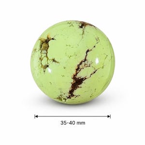 May include: A polished, spherical gemstone in a pale green hue, with dark brown veining and inclusions. The sphere measures 35-40 mm in diameter. The stone is set against a white background, highlighting its natural beauty and unique patterns.
