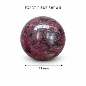 Puede incluir: Una gema esférica pulida, principalmente de color rojo intenso con vetas e inclusiones más oscuras. La esfera tiene 4,1 cm de diámetro. El texto "EXACT PIECE SHOWN" está en la parte superior. La gema está sobre un fondo blanco.