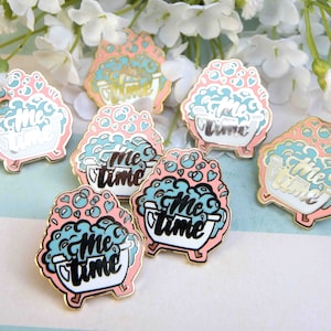 May include: Six enamel pins featuring a bathtub with bubbles and the text "Me Time" in black. The pins are pink, white, and blue.