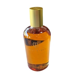 May include: A clear glass bottle filled with amber-colored liquid, featuring a gold-toned cylindrical cap. The front of the bottle displays a gold logo with the text Claire Burke printed in a clean, sans-serif font centered on the glass surface.