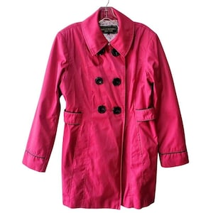 May include: A bright pink double-breasted coat with black buttons and black trim. The coat has a classic collar and two front pockets. The label reads "Maison Richards New York".