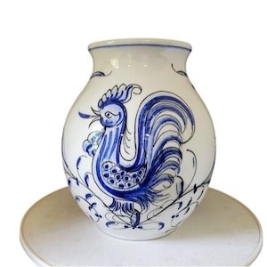 May include: White ceramic vase with a hand-painted blue rooster design. The vase has a rounded body and a flared rim, with floral accents. A decorative piece for home decor.
