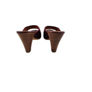 May include: A pair of burgundy leather slip-on mules with wooden cone heels. The open-toe design features a single strap across the top of the foot. The heels are approximately 3 inches tall.