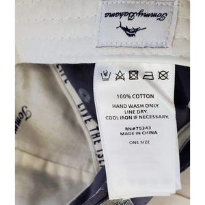 May include: Close-up of a white tag with care instructions and the text "100% COTTON." The tag also includes the text "HAND WASH ONLY. LINE DRY. COOL IRON IF NECESSARY." The tag is attached to a garment.
