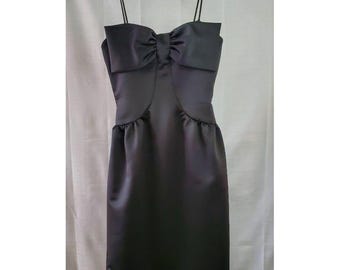 May include: A black satin dress with a bow at the neckline. The dress has a fitted bodice and a full skirt.