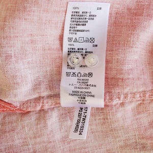 May include: A white care label with black text and symbols. The label includes washing instructions, fabric content, and manufacturer information. The text includes "100% Linen", "Made in China", "Fabrique en Chine", "RN 86549", "CA 58297", "Tommy Bahama", and "PO 237155(4525)".