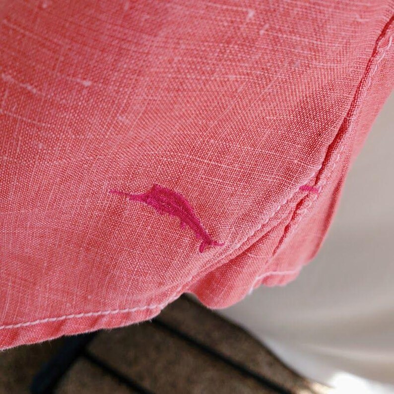 May include: A coral pink linen shirt with a pink embroidered dolphin design.