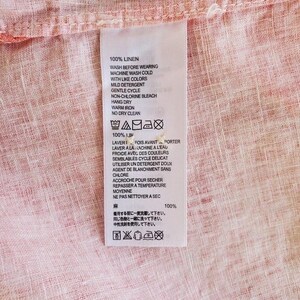 May include: A white care label with instructions for washing, drying, and ironing a linen garment. The label includes text in English, French, and Japanese. The label is attached to a pink linen fabric.