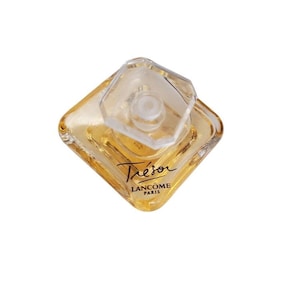 Puede incluir: Un frasco de perfume de vidrio transparente con base cuadrada y tapón transparente facetado. El frasco contiene un líquido de color dorado. La palabra "Trésor" está escrita en cursiva, con "Lancôme Paris" debajo.