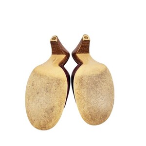May include: A pair of burgundy-colored high heels, viewed from the soles. The heels are a dark brown color, and the soles are a light tan with wear marks. The shoes are set against a white background.
