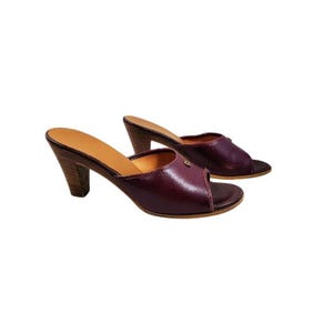 May include: A pair of burgundy leather open-toe heeled mules. The shoes have a wooden heel and a light brown insole. The heels are approximately 3 inches tall.