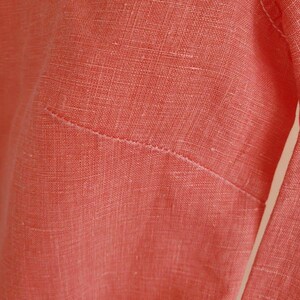 May include: Close-up of a coral-coloured linen fabric with a visible seam.