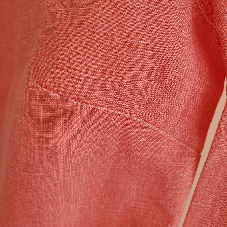 May include: Close-up of a coral-coloured linen fabric with a visible seam.