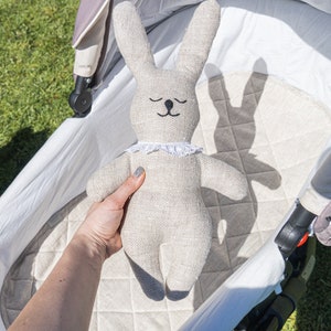 May include: A beige linen bunny rabbit toy with black eyes and a white lace collar is in a white pram.