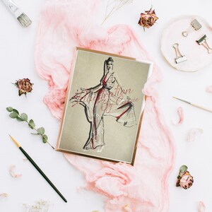 Könnte beinhalten: Eine gerahmte Illustration einer Frau in einem weißen Kleid mit roten Akzenten. Die Illustration ist auf braunem Hintergrund und der Rahmen ist golden. Die Illustration ist von rosa Stoff und anderen Dekorationsartikeln umgeben.