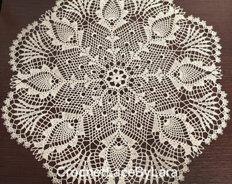 May include: Cream-coloured, circular crocheted doily with an intricate lace pattern. The doily features a central floral design surrounded by detailed openwork and scalloped edges. The text "CrochetLaceByLara" is visible at the bottom.
