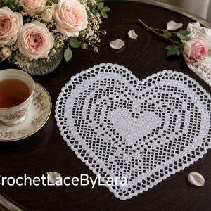 May include: A white heart-shaped crochet doily featuring an intricate openwork pattern with a central heart motif and a scalloped border. The text CrochetLaceByLara is printed in white at the bottom of the image.