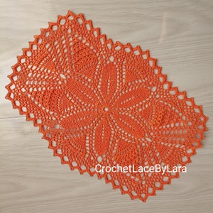 Może przedstawiać: Koronkowa serwetka w kolorze pomarańczowym z delikatnym wzorem kwiatowym. Serwetka jest prostokątna i ma falowany brzeg. Tekst "CrochetLaceByLara" jest widoczny w prawym dolnym rogu.