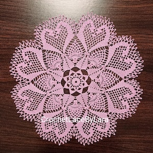 Könnte beinhalten: Eine zarte rosa Häkeldeckchen mit einem floralen Design. Die Deckchen hat eine sternförmige Mitte und komplizierte Häkelarbeiten.